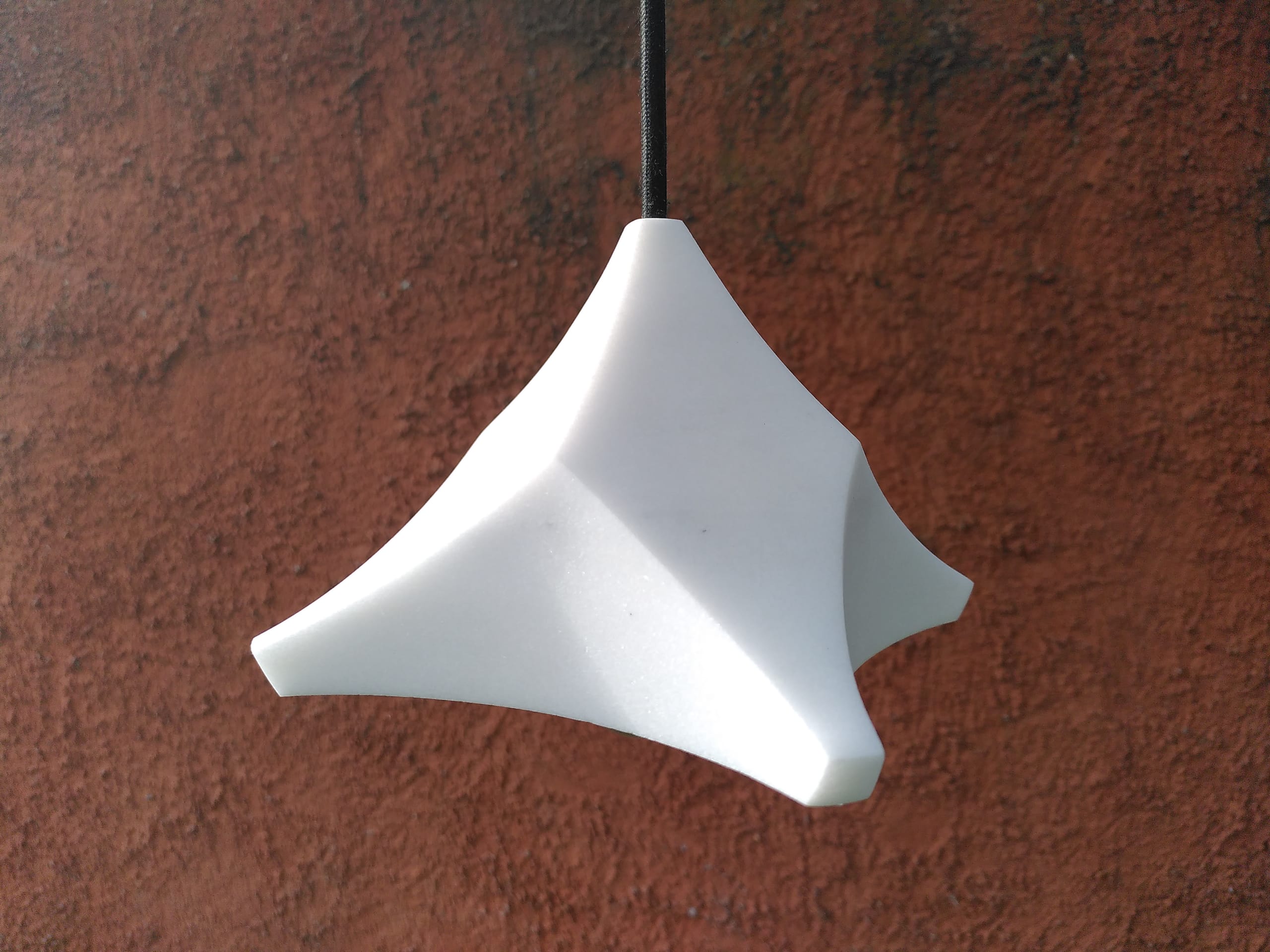 Die fertige Lampe hängt vor einer rotbraunen Lehmwand, die vier Zipfel nach unten gezogen