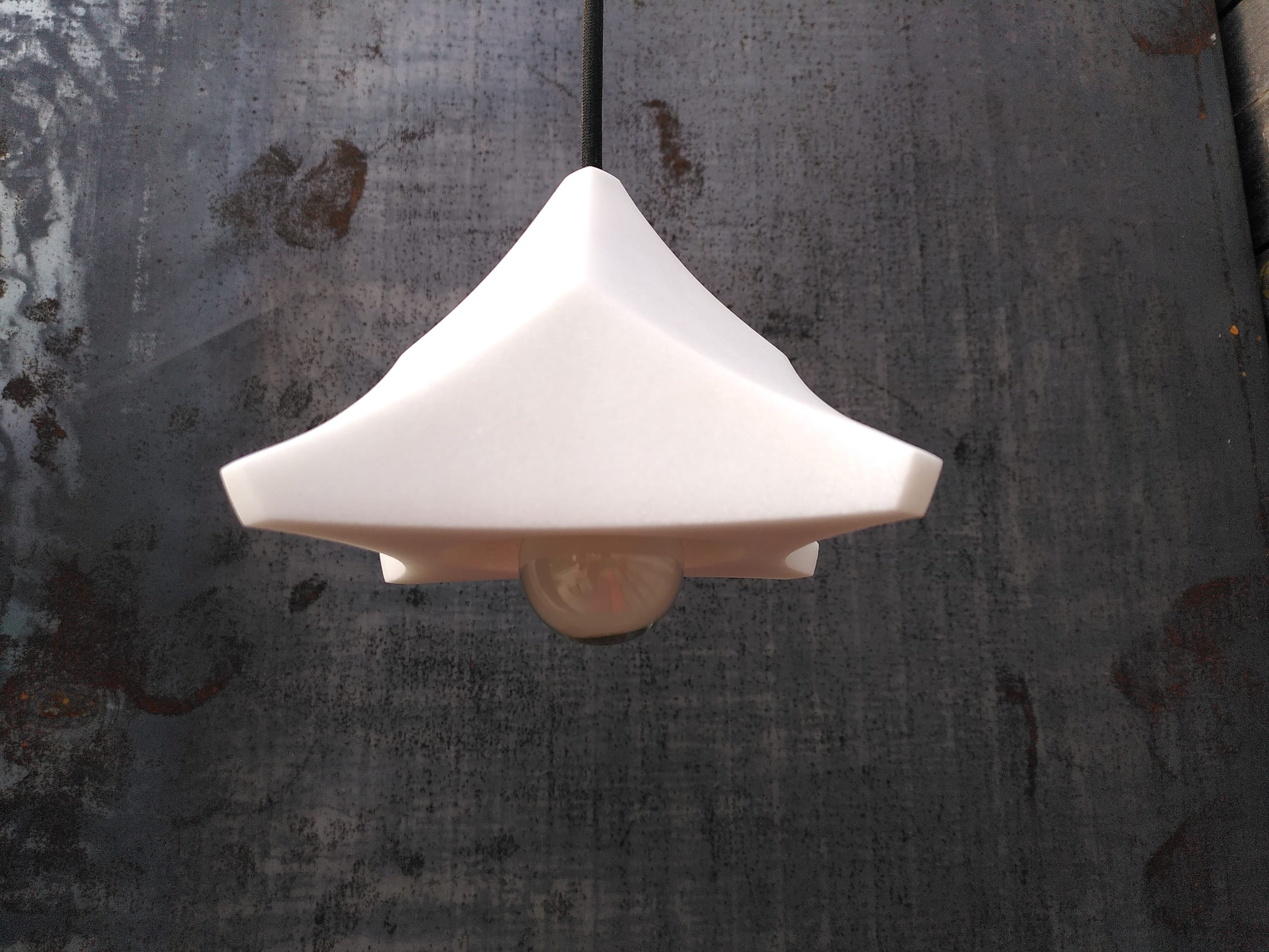 Die Lampe von unten vor einer dunklen Betonwand, die Fassung in der Mitte sichtbar